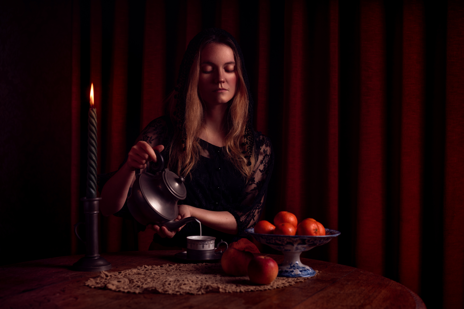 Photographie portrait à la bougie d'une femme versant du lait dans une petite tasse. Une coupe de fruits est disposée sur la table.